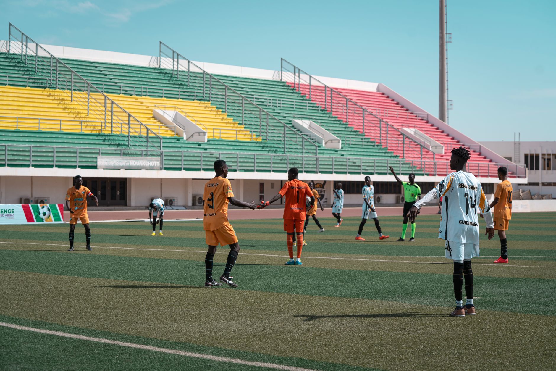 Match de football énergique avec des joueurs en orange et blanc, sur fond de stade vibrant.