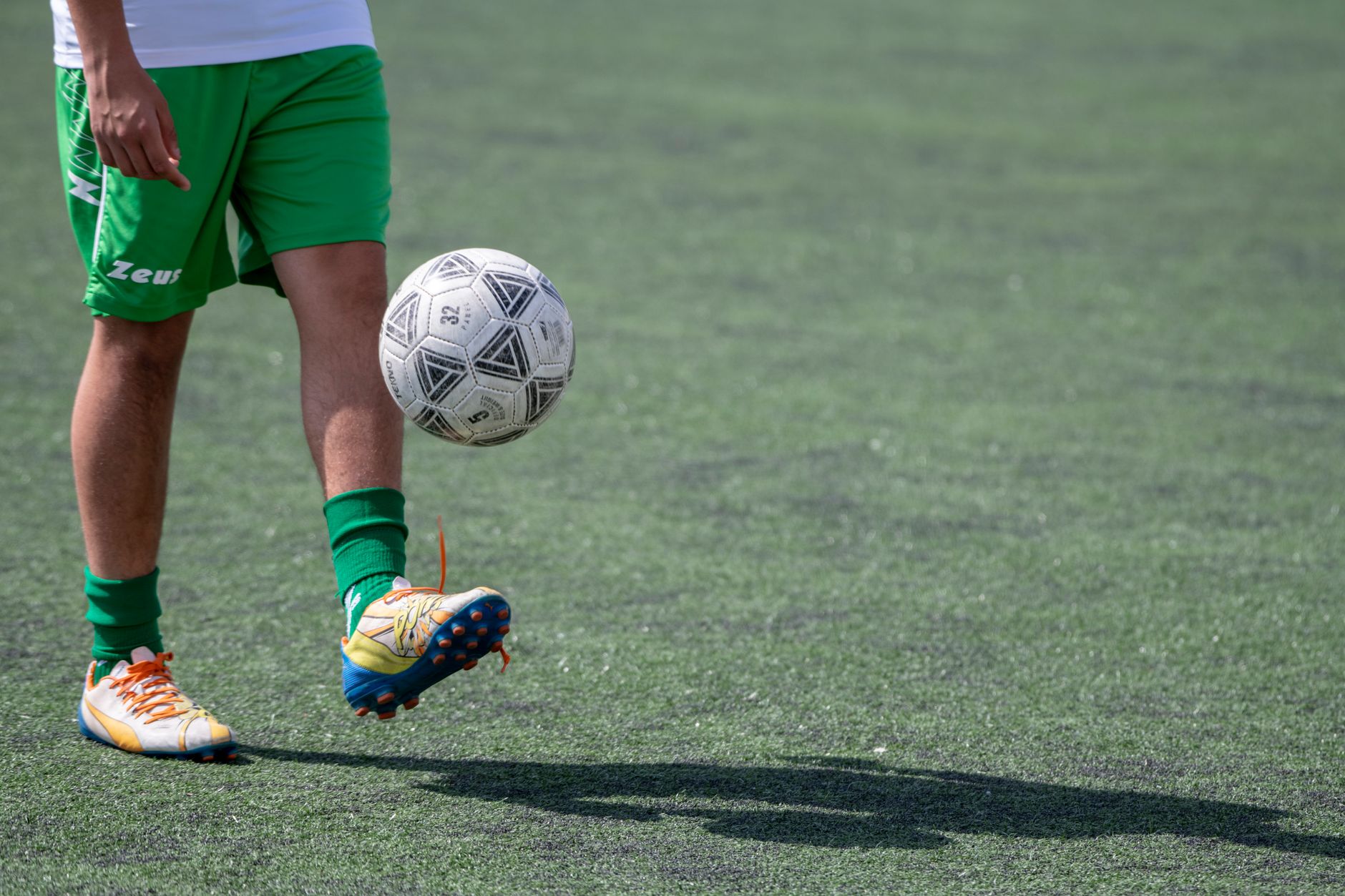 Gros plan sur des jambes en tenue verte, un pied levé sous un ballon de football.