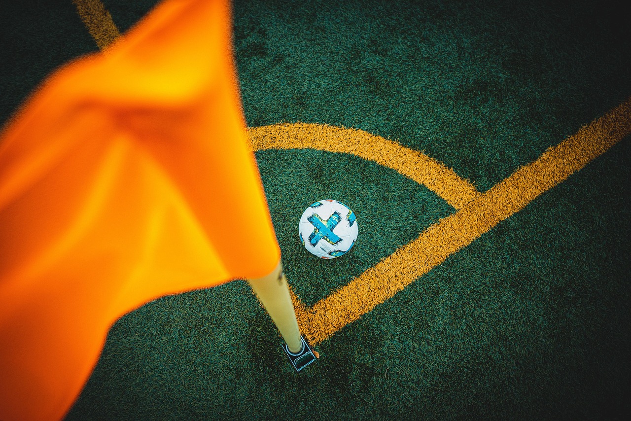Drapeau de corner orange et ballon de football près de l'arc de coin sur une pelouse synthétique